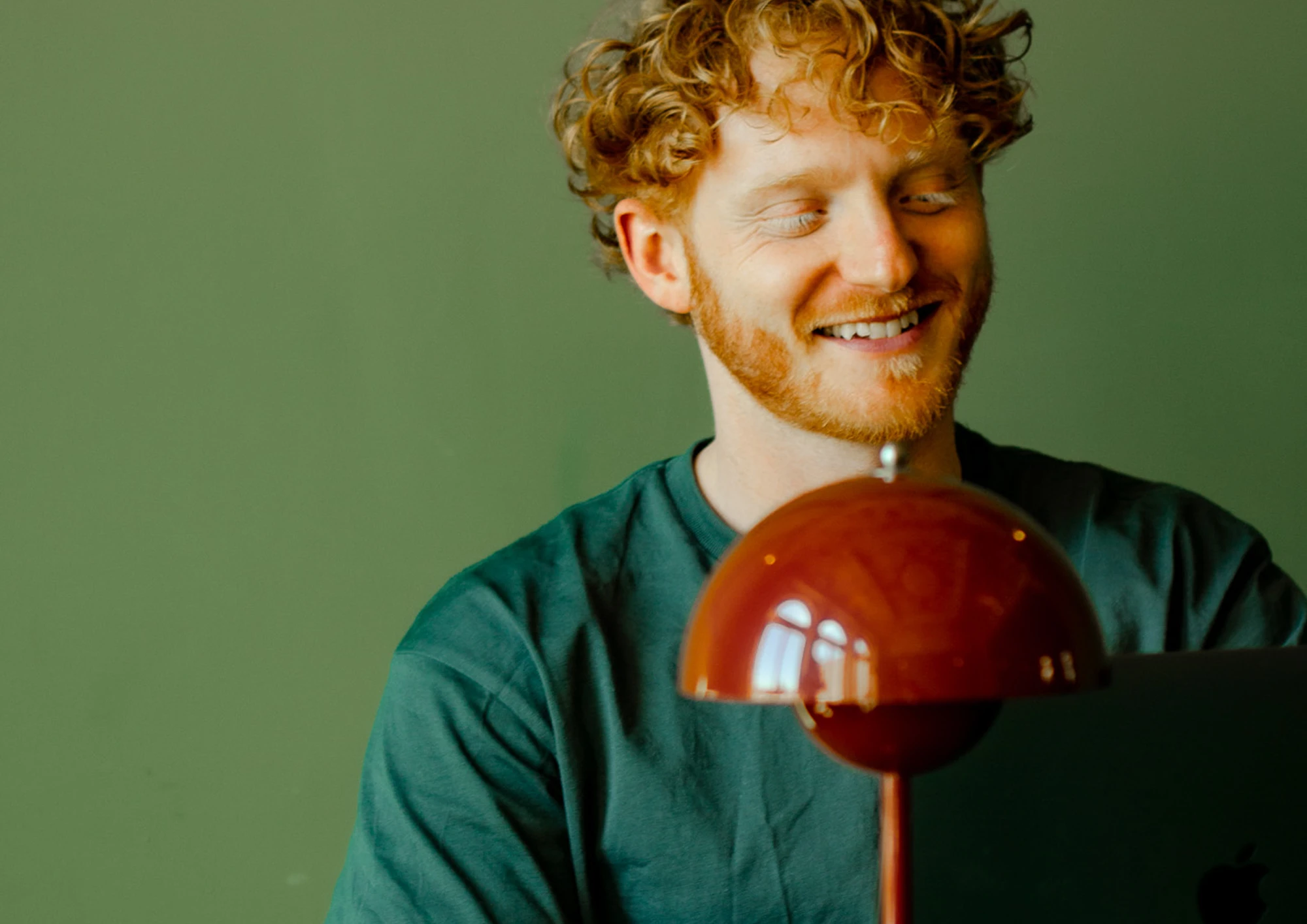 Joe, smiling at a laptop against a green wall
